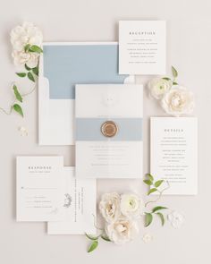 the wedding stationery is laid out on top of each other with white flowers and greenery