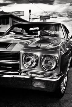 a black and white photo of an old car parked in front of a gas station