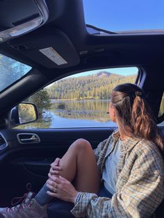 a woman sitting in the passenger seat of a car next to a lake and mountains