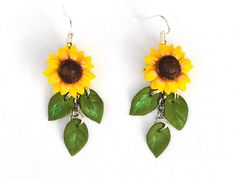 two sunflowers with green leaves are hanging from the ear hooks on white background