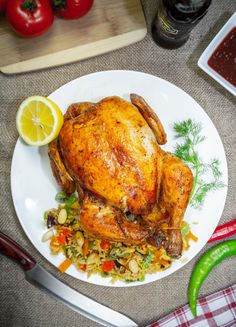 a whole chicken sitting on top of a white plate next to a knife and fork