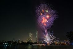 fireworks are lit up in the night sky over a body of water with city lights