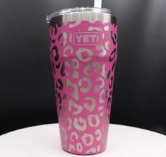 a pink leopard print tumbler cup sitting on top of a white table with a straw in it