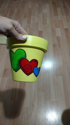 a hand holding a yellow cup with hearts painted on it