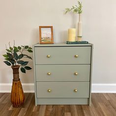 a green dresser next to a vase with plants on top