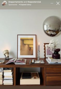 a wooden desk topped with books next to a mirror and vase filled with white flowers