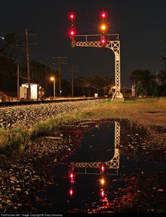 a railroad crossing with red lights reflecting in the wet ground and grass on either side