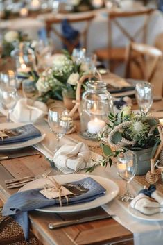 the table is set with white and blue flowers, greenery, candles and napkins