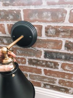 a person is holding a black lamp in front of a brick wall and pointing it at the light