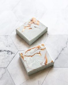 two marble coasters with gold leaf designs on them sitting on a white tile floor