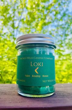 a green candle sitting on top of a wooden table next to some trees and bushes