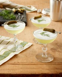 two martinis with dill garnish sit on a table next to silverware