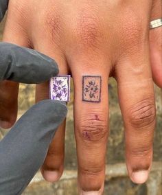 a person's left hand with a small tattoo on the middle finger and purple flowers