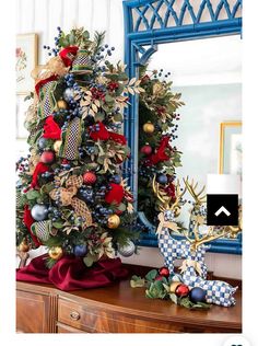 a christmas tree decorated with red, blue and gold ornaments in front of a mirror