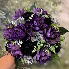 a bridal bouquet with purple flowers and greenery is held by a woman's hand