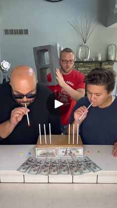 two men and a woman blowing out candles on a cake with money in front of them