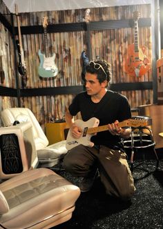 a man is playing an electric guitar in a room with guitars on the wall behind him