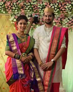 a man and woman standing next to each other in front of a flower covered wall