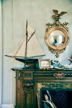 a sailboat sitting on top of a mantle next to a mirror and fire place