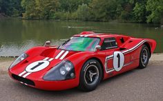 a red race car parked next to a lake