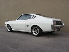 a white muscle car parked in front of a tan wall with no door on it