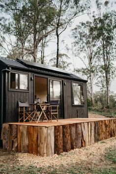 a tiny cabin with wooden deck and table on the outside, surrounded by trees in the background