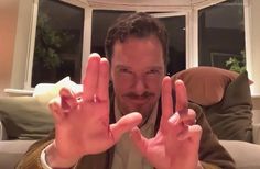 a man is making the peace sign with his hands while sitting on a couch in front of a window