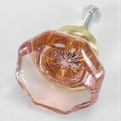 a pink and gold glass object with a screw in the middle on a white surface