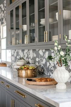 a kitchen with gray cabinets and white flowers on the countertop, along with gold trim