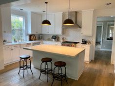 a kitchen with two stools in front of an island and three lights hanging from the ceiling