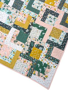 a patchwork quilt is laying on top of a white surface with pink, green and yellow squares