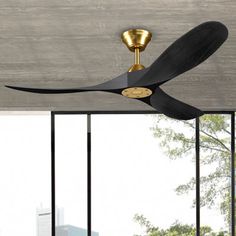 a black ceiling fan with gold accents in a room next to large windows and a cityscape