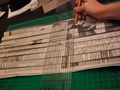 a person is cutting out newspaper pieces on a green mat with a pair of scissors