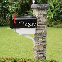 a mailbox in the middle of a flower bed with grass and trees behind it