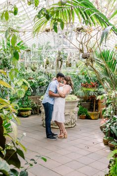 an engaged couple embraces in the middle of a greenhouse filled with potted plants