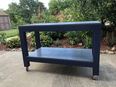 a blue table sitting on top of a cement ground next to bushes and trees in the background