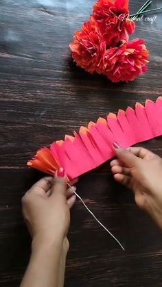 someone is making a paper flower out of pink and orange flowers on a wooden table