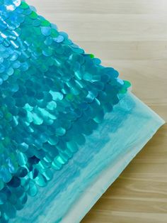 blue and green sequinized fabric sitting on top of a wooden table