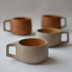 three coffee cups sitting on top of a white table next to two mugs with handles