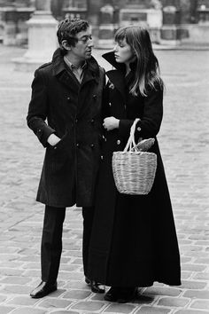 a man and woman standing next to each other on a brick road with a basket in their hand