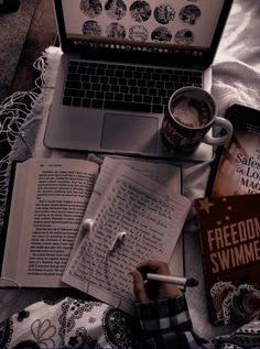 a laptop computer sitting on top of a bed next to a cup of coffee and books