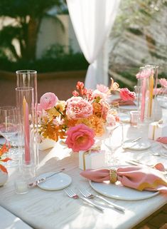 the table is set with pink and orange flowers in vases, napkins, and candles