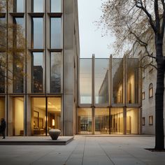 an empty courtyard in front of a building with glass walls and trees on both sides