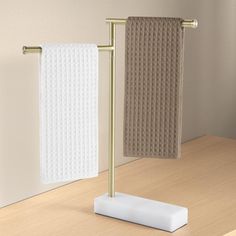 two towels are hanging on a towel rack next to a white towel holder with gold handles