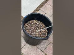 a black bucket filled with dirt sitting on top of a sidewalk