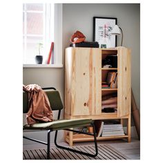 a wooden cabinet sitting next to a window in a room with a chair and bookshelf