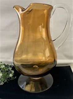 a brown glass pitcher sitting on top of a table next to a white flower arrangement