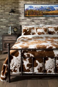 a bed with brown and white cow print comforter in a bedroom next to a brick wall