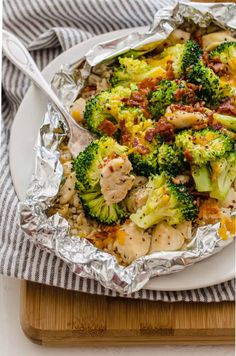 a white plate topped with chicken and broccoli covered in tin foil on top of a wooden cutting board