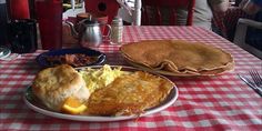 a table topped with plates of breakfast food and pancakes on top of a red checkered table cloth